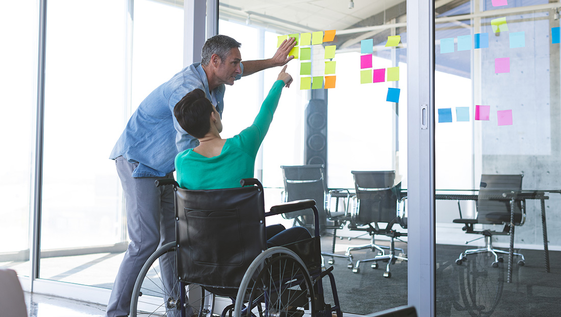 Recruiting disabled students: a woman in a wheelchair discussing over sticky notes on glass with her colleague