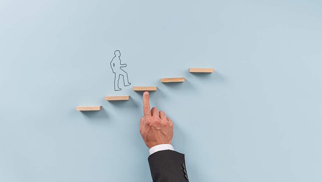 Graduate development: Hand of a businessman supporting wooden step for a silhouetted man to walk upwards