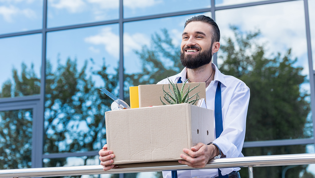 young people quitting jobs: a happy employee carrying a cardboard box with office supplies