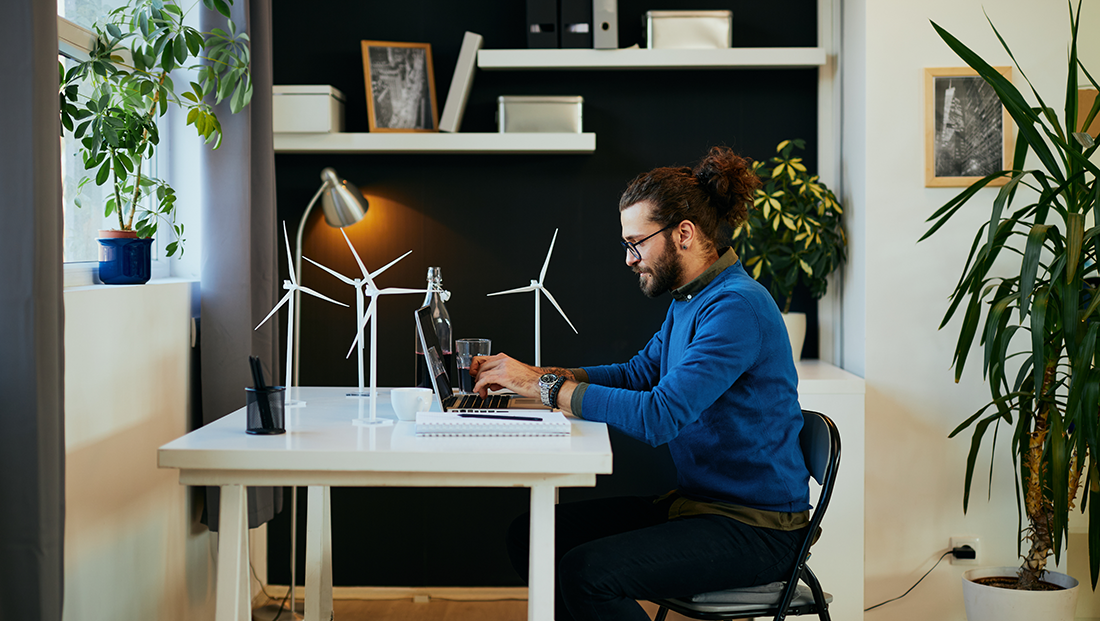 sustainability careers: male employee working in his office with wind farm models on the desk, surrounded by plants