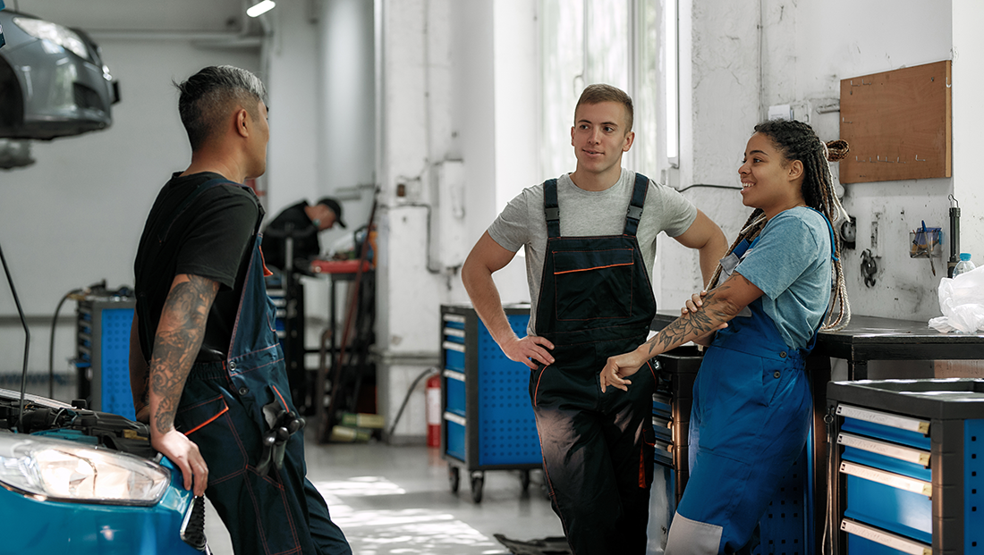 socially diverse apprentices: team of diverse mechanics in uniform, two men and a woman talking